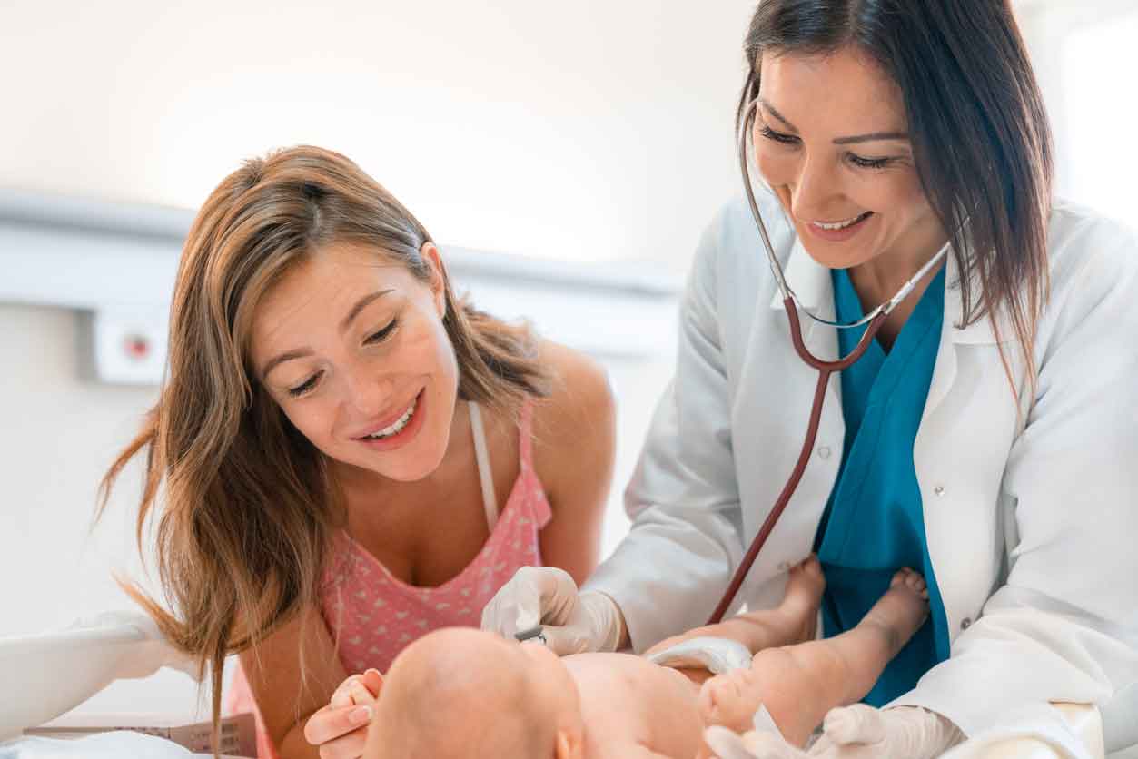 Smiling female pediatrician examining newborn baby with stethoscope while the mother is standing next to her.
